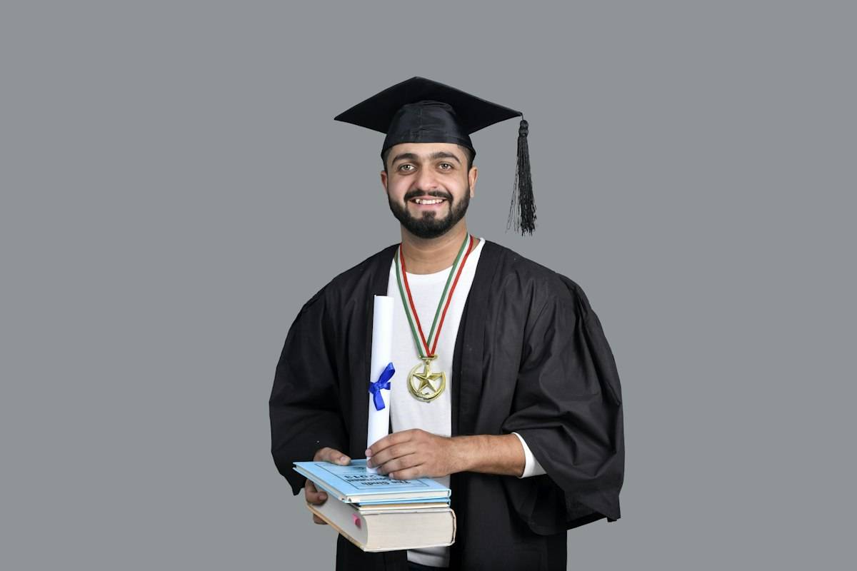 مرد فارغالتحصیل با کلاه و لباس دانشگاهی و کتاب؛ تصویر مرتبط با ادامه تحصیل